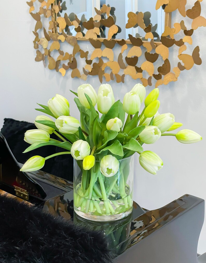 May include: A clear glass vase filled with white and yellow tulips. The vase is sitting on a black surface.