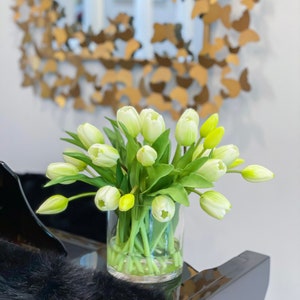 May include: A bouquet of white tulips with green stems in a clear glass vase. The vase is sitting on a black surface.