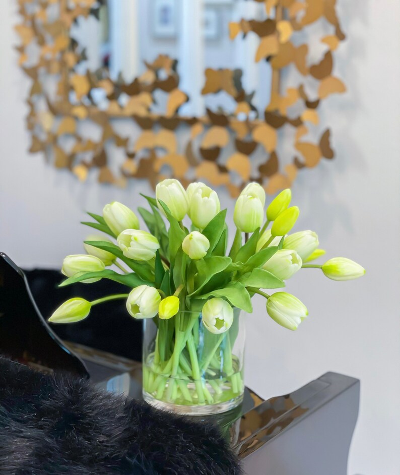 May include: A bouquet of white tulips with green stems in a clear glass vase. The vase is sitting on a black surface.