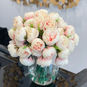 May include: A bouquet of pale pink peonies arranged in a clear glass vase. The vase is sitting on a black surface.