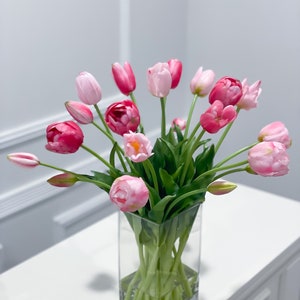 Puede incluir: Un ramo de tulipanes rosas y blancos arreglados en un jarr&oacute;n de vidrio transparente. El jarr&oacute;n est&aacute; sobre una mesa blanca.