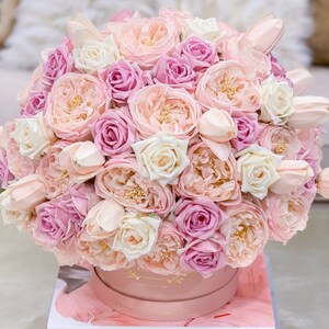 Puede incluir: Un arreglo floral de rosas, peon&iacute;as y tulipanes en una caja rosa. Las flores son de color rosa y blanco.