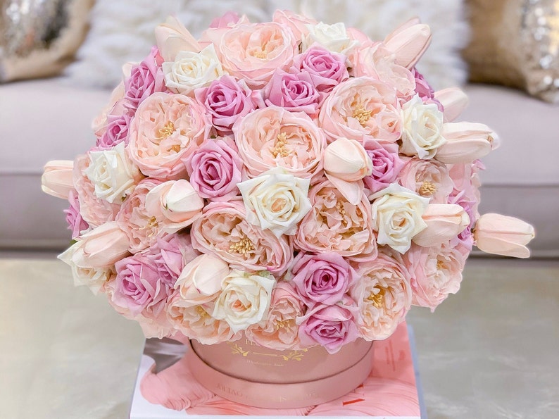 Puede incluir: Un arreglo floral de rosas, peon&iacute;as y tulipanes en una caja rosa. Las flores son de color rosa y blanco.