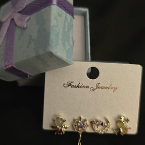 May include: A set of four gold-tone stud earrings on a white display card labeled Fashion Jewelry. The designs include a bat with a stone, a spider web with a dangling spider, a crescent moon with a purple stone, and a witch hat with a green stone.