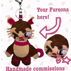 May include: A brown and tan felt plush keychain featuring a stylized character with a pink scarf, pink accents, and a metal keyring. The image includes the text Your Fursona here! with an arrow pointing to the character and Handmade commissions.