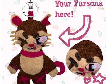 Puede incluir: Un llavero de fieltro marrón y beige con un personaje estilizado, una bufanda rosa, detalles en rosa y una anilla de metal. La imagen incluye el texto Your Fursona here! con una flecha y la frase Handmade commissions.