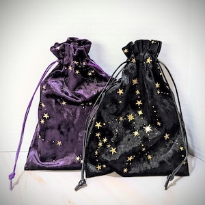 May include: Two velvet drawstring bags with gold star patterns. One bag is purple and the other is black.