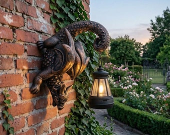 May include: A bronze-colored wall-mounted dragon sculpture featuring a textured, scaled body and wings. The dragon's tail curves upward to hold a black, lantern-style light fixture with a glowing bulb, creating a decorative outdoor wall accent.