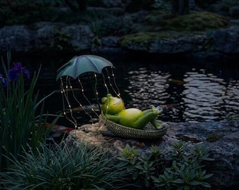 May include: A green frog figurine resting in a woven basket under a dark green umbrella. The umbrella is adorned with thin, glowing string lights that drape down like rain, illuminating the frog as it lies back in a relaxed, reclining position.