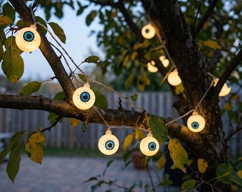 May include: A string of decorative lights featuring spherical bulbs designed to resemble eyeballs. Each white globe has a blue iris and a black pupil in the center. The lights are connected by a thin wire and are illuminated, casting a soft glow.