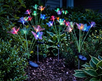 May include: Multiple solar-powered garden stakes featuring translucent, multi-colored butterfly-shaped light fixtures. Each stake has thin green stems and a small solar panel base, emitting glowing blue, pink, and orange light in the dark.
