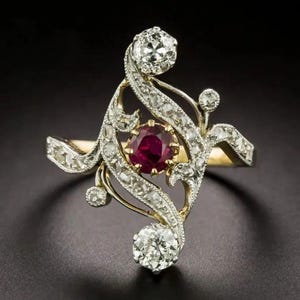 Peut inclure: Une bague en or ornée d'un rubis rouge central taille ronde, entouré d'une monture ajourée en métal torsadé sertie de multiples petits diamants blancs ronds. Le design comprend deux diamants ronds plus grands aux extrémités.