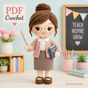 Può includere: Una bambola all'uncinetto con capelli castani raccolti in uno chignon, indossa un cardigan rosa, una camicia bianca con colletto e una gonna marrone. La bambola ha occhiali tondi, tiene un puntatore in legno e un libro blu con scritto Lessons.