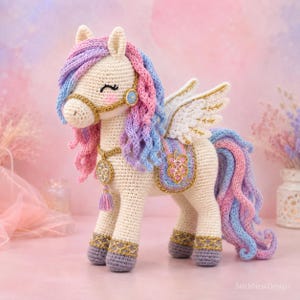 Könnte beinhalten: Ein cremefarbenes gehäkeltes Pegasus-Spielzeug mit einer Mähne und einem Schweif in Rosa-, Lila- und Blautönen. Die Figur hat weiße Flügel mit Goldstickerei, ein dekoratives Zaumzeug mit Quaste und violette Hufe mit goldenen Akzenten.