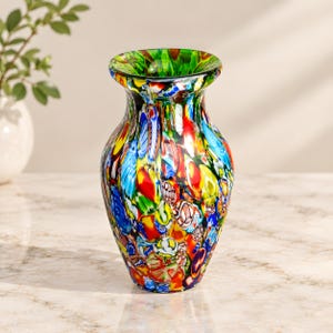 Puede incluir: Un florero de vidrio con un vibrante patrón millefiori en una multitud de colores, incluyendo rojo, azul, amarillo y verde. El florero tiene un cuerpo redondeado que se estrecha hacia una abertura ensanchada con borde verde.