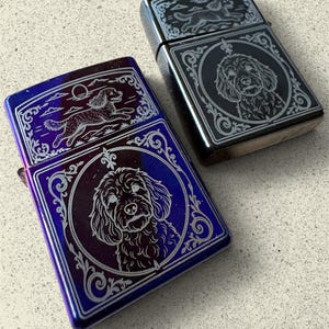 Peut inclure: Deux briquets métalliques rectangulaires ornés de portraits de chiens gravés. L'un présente une finition irisée violette et bleue, l'autre une finition noire métallique sombre. Les deux montrent un visage de chien dans un cadre circulaire.