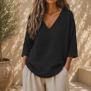 May include: A solid black V-neck top with three-quarter length sleeves and a relaxed fit, paired with light beige trousers. The top features a simple design with a deep neckline and loose silhouette, providing a clean and straightforward appearance.