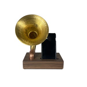 May include: A unique phone stand featuring a brass horn speaker design. The stand includes a dark brown wooden base and a black phone holder. The horn is gold-colored, and the stand has a vintage aesthetic.