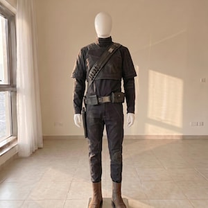 Pu&ograve; includere: Una maglia a maniche lunghe grigio scuro e pantaloni abbinati indossati da un manichino. L'outfit include una tracolla grigio scuro con tasche, una cintura con due tasche rettangolari, una fondina e stivali marroni effetto pelle.