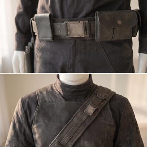 Pu&ograve; includere: Una cintura multiuso grigio scuro con fibbia metallica e due tasche rettangolari, abbinata a un'imbracatura pettorale coordinata che presenta una tracolla diagonale con un dettaglio metallico e diversi piccoli passanti.
