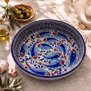 May include: A round ceramic bowl featuring a hand-painted pattern of blue fish with red accents on a white background, surrounded by small blue dots. The interior rim is decorated with a repeating geometric border in blue, red, and white.