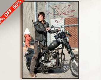 May include: A framed photographic print featuring a person with dark hair wearing a black leather jacket and brown pants, sitting on a black motorcycle. The image includes a red handwritten signature and a red diagonal banner stating 50% OFF.