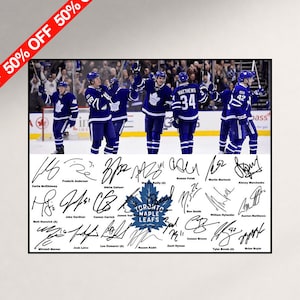 Può includere: Una stampa rettangolare con una fotografia di giocatori di hockey dei Toronto Maple Leafs in uniformi blu e bianche che festeggiano sul ghiaccio, sopra una sezione bianca contenente il logo della squadra e diverse firme a inchiostro nero.