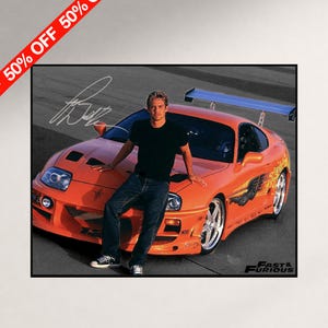 May include: A photographic print featuring a person in a black t-shirt and blue jeans leaning against an orange sports car with a rear spoiler and custom decals. The image includes a white signature and the text Fast & Furious in the corner.