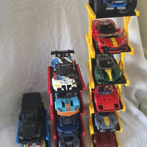 May include: A collection of toy car models displayed on three vertical plastic storage racks. The racks hold various sports cars, SUVs, and racing vehicles in red, yellow, blue, black, and green, featuring detailed designs and small plastic wheels.