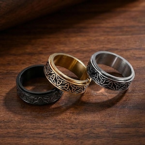May include: Three metal rings featuring a continuous engraved Celtic knot pattern. The set includes one black ring, one gold-tone ring, and one silver-tone ring. Each band has a wide, flat profile with a repeating triangular geometric design.