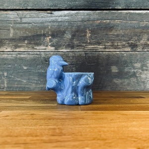 以下が含まれることがあります： 鳥が乗った木の切り株の形をした青いセラミック製のプランター。プランターは素朴で風化した外観をしています。