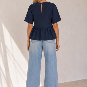 May include: A dark navy blue short-sleeved peplum top featuring a round neckline with a small keyhole cutout and a single button closure at the back, paired with light blue wide-leg denim jeans that have a classic five-pocket design.