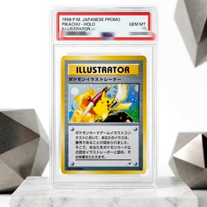 May include: A PSA graded 1998 Japanese promo Pikachu Illustrator trading card in a clear plastic slab. The card features a yellow Pikachu holding a paintbrush and pen, with Japanese text and the word ILLUSTRATOR printed in a bold yellow header.