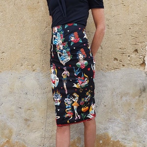 Peut inclure: Une jupe crayon noire avec un imprimé de tatouage coloré représentant des cœurs, des fleurs et des femmes. La jupe a une bordure rouge et est associée à des chaussures à plateforme noires.