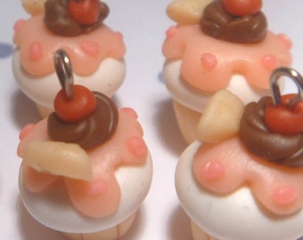 May include: Miniature cupcake charms with pink frosting, chocolate swirls, a cherry, and a silver loop for jewelry making. The cupcakes have a white base and are decorated with small, light-colored pieces.