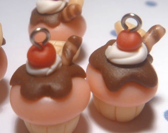May include: Four miniature cupcake charms. Each charm features a pink base, chocolate frosting, white cream, a red cherry, and a small wafer. The charms have a silver loop for attaching to jewelry or other crafts.