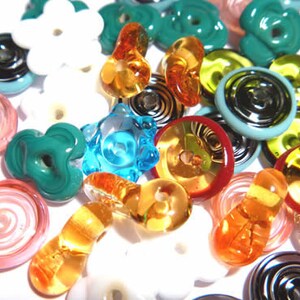 May include: A collection of colorful glass beads in various shapes and sizes. The beads include flower, spiral, and button designs in shades of white, blue, green, orange, and red. Some beads have a glossy finish, while others are translucent.