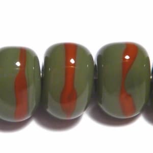 May include: Close-up of olive green beads with a vertical red stripe. The beads are smooth and glossy, with a rounded rectangular shape. The beads are strung together, and the background is white.