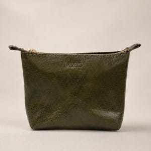 May include: A small olive green leather pouch with a textured finish and visible stitching along the top edge. The bag features a gold-toned metal zipper closure and the word MOREL embossed in the centre of the front panel.