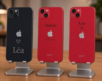 May include: Three smartphones displayed on silver metal stands. The left phone is black with the name Léa and a heart icon. The middle phone is red with the name Simon and the date 12.04.2021. The right phone is red with the name Léa and a heart icon.
