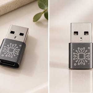 May include: A dark grey USB-A to USB-C adapter featuring a white laser-engraved circuit board pattern on the casing. The metallic connector end is silver, while the main body displays a detailed schematic design of a central processor chip.