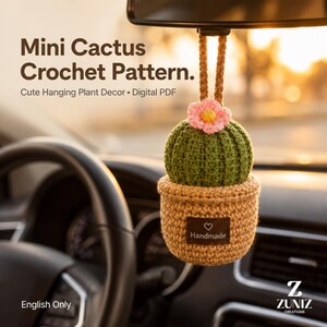 Pode incluir: Um ornamento suspenso de mini cacto em crochê com corpo verde, uma flor rosa com centro amarelo e um vaso bege. Uma etiqueta retangular marrom no vaso apresenta um ícone de coração branco e o texto Handmade. O texto Mini Cactus Crochet Pattern. Cute Hanging Plant Decor • Digital PDF é visível.