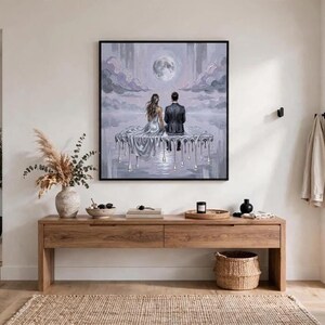 A large, framed oil painting of a couple on a dripping silver platform under a full moon hangs above a wooden console table in a minimalist room with a potted plant.