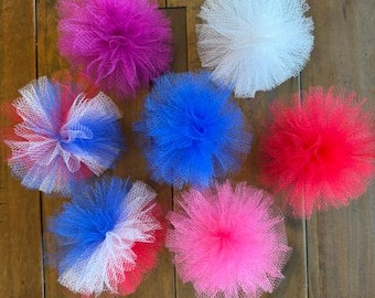 May include: Seven round tulle pom-poms in various colors including solid magenta, white, blue, and red, along with multi-colored combinations of red, white, and blue. Each pom-pom features a dense, layered mesh texture arranged in a circular shape.
