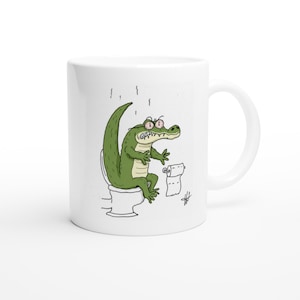 Può includere: Una tazza in ceramica bianca con un'illustrazione a cartoni animati di un coccodrillo verde con gli occhi iniettati di sangue seduto su un water bianco. Il coccodrillo ha un'espressione angosciata accanto a un rotolo di carta igienica.