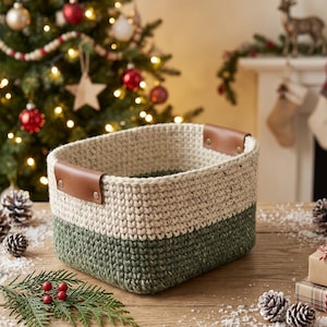 May include: A rectangular storage basket featuring a two-tone design with a cream-coloured upper section and a dark green lower section. The basket is constructed from thick, textured yarn and includes two brown faux leather handles attached with rivets.