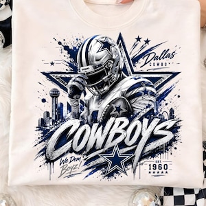 May include: A cream-colored crewneck sweatshirt featuring a graphic of a football player in a helmet and uniform, a large star, the Dallas skyline, and the text "Dallas Cowboys", "Cowboys", "We Dem Boyz!", and "Est. 1960" in blue and white.