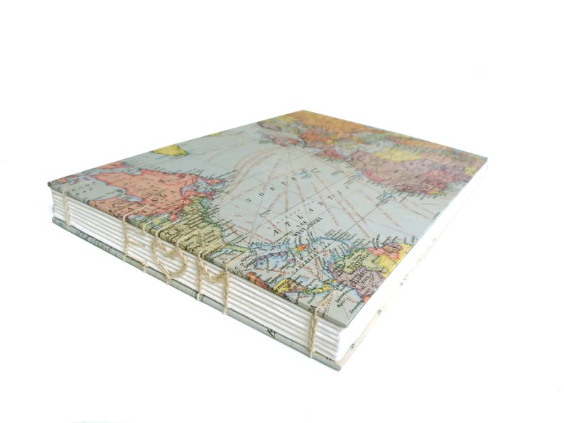 May include: A square book with a vintage map print cover featuring the North Atlantic Ocean. The book has exposed coptic stitching along the spine, utilizing thick, light-colored thread to bind the white paper pages together in a visible pattern.