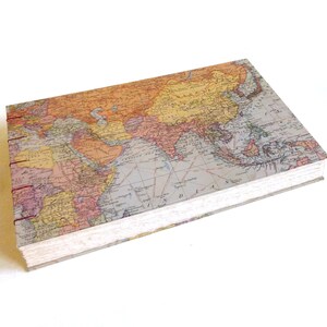 May include: A rectangular hardcover journal featuring a vintage-style world map print on the cover. The book is bound with exposed dark red stitching along the spine, showcasing a detailed cartographic design with muted orange, tan, and blue tones.
