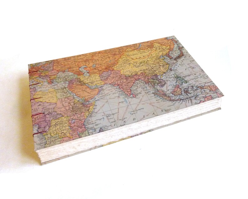 May include: A rectangular hardcover journal featuring a vintage-style world map print on the cover. The book is bound with exposed dark red stitching along the spine, showcasing a detailed cartographic design with muted orange, tan, and blue tones.